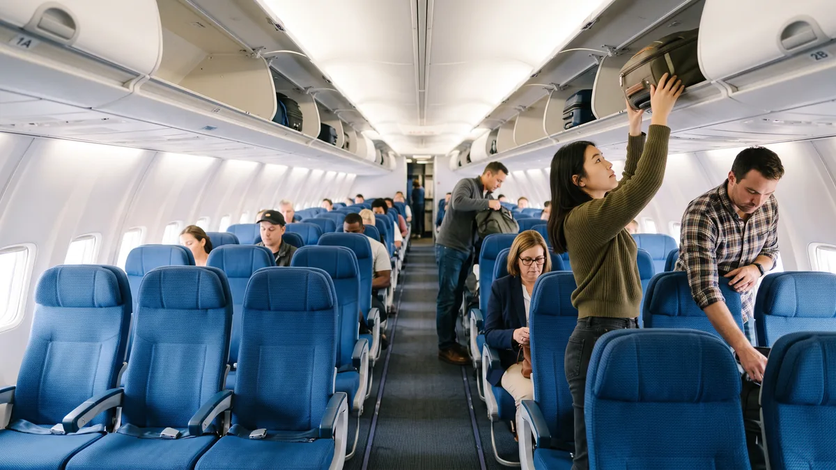 La cabina económica de un avión vista desde el pasillo, con pasajeros acomodándose