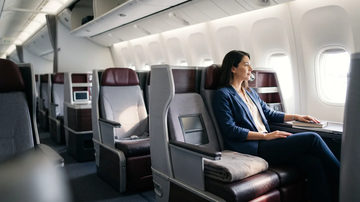 La cabina business de un avión vista desde el pasillo, con un pasajero acomodándose